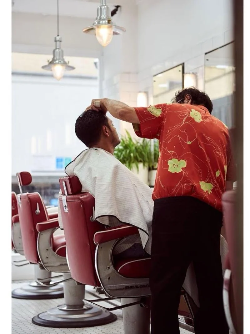 Barber trimming a client's hair in a red floral shirt